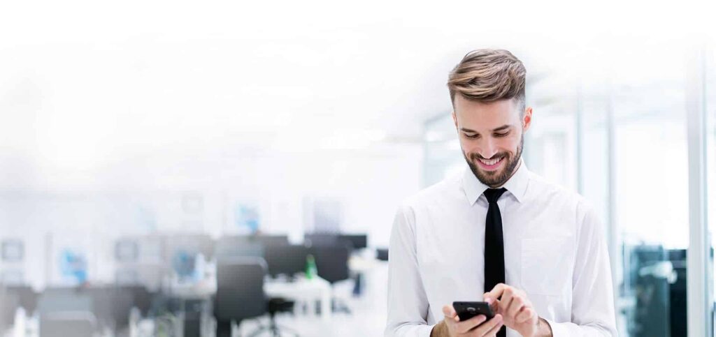 Smiling professional checking his phone in a modern open-plan office