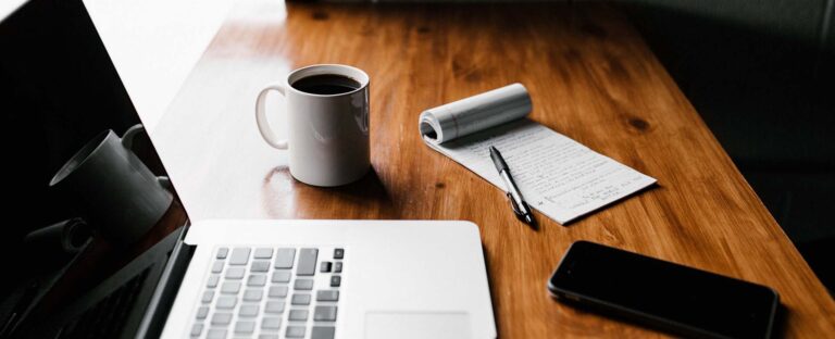 Laptop, coffee cup, notepad and phone on a wooden desk