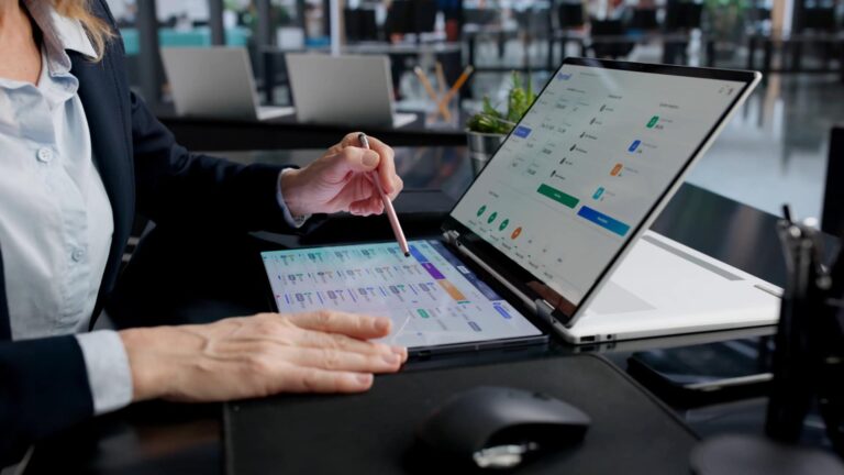 Woman using a stylus on a tablet next to a laptop showing a dashboard