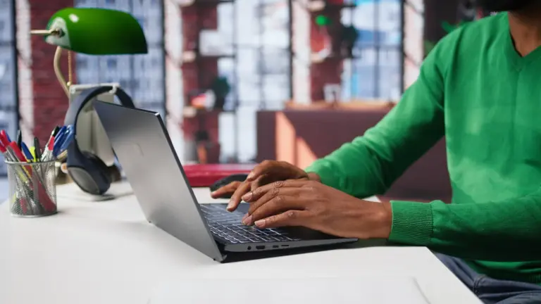 Person in a green jumper typing a blog post on a laptop