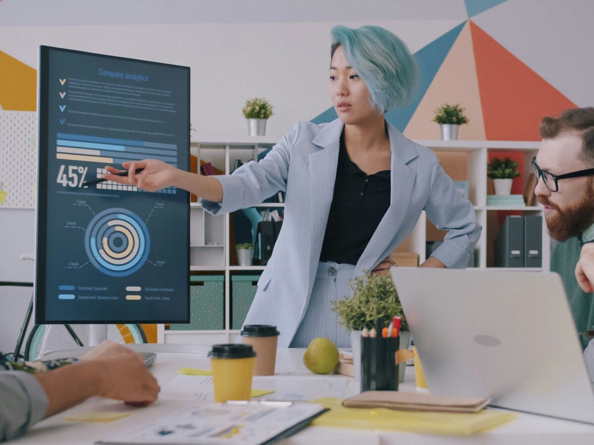 Strategist presenting a data dashboard on a large screen to colleagues around a table