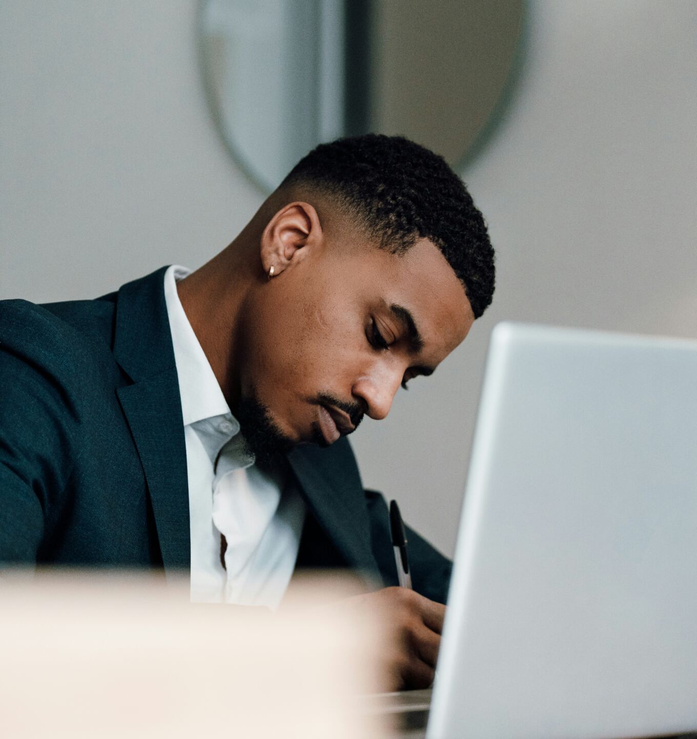 Professional in a suit writing notes beside his laptop