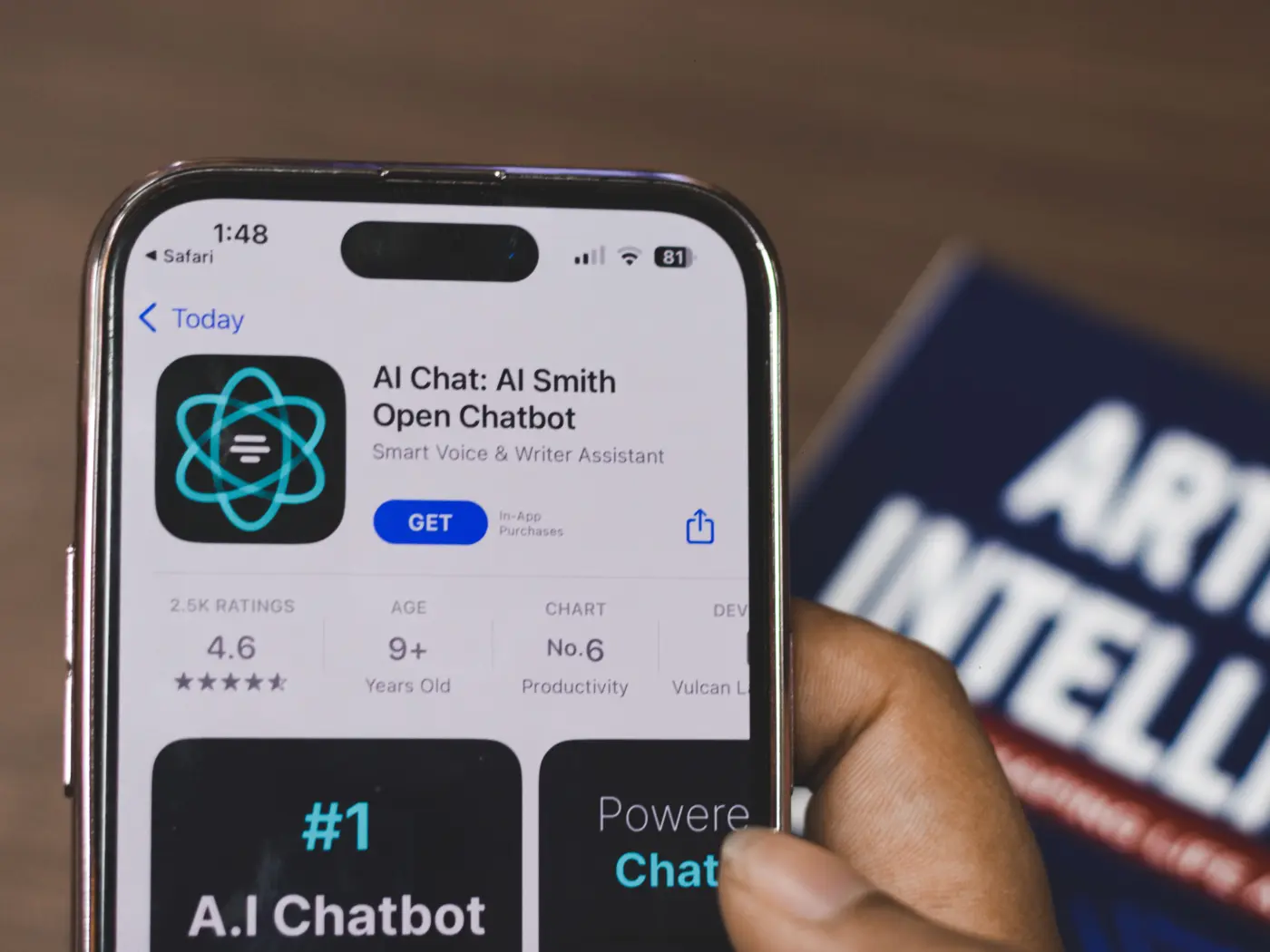 Phone showing an AI chatbot app in the app store, held beside a book about artificial intelligence