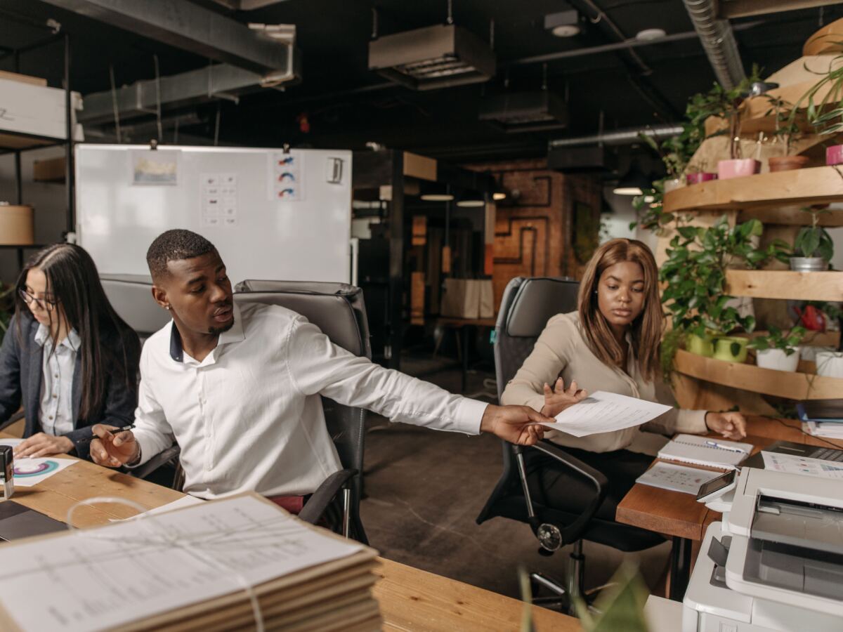 Colleagues passing documents across a shared desk in a busy office