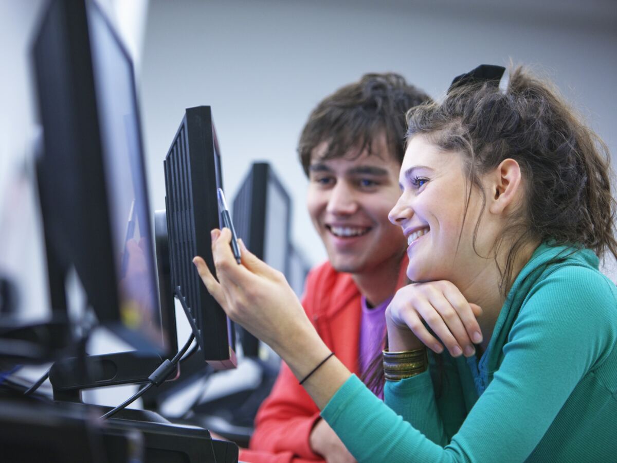 Two colleagues smiling at a monitor as they review work together