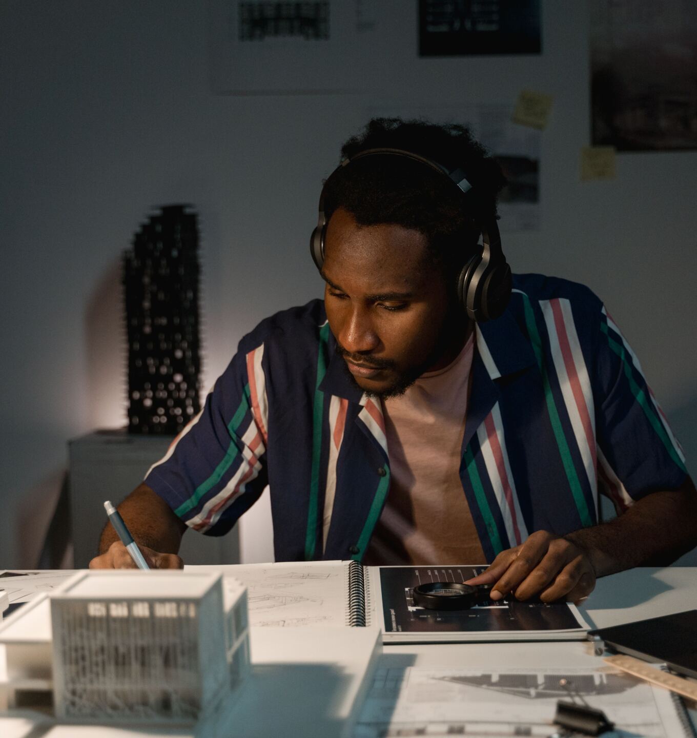 Creative working at a desk with headphones on, sketching beside an architectural model
