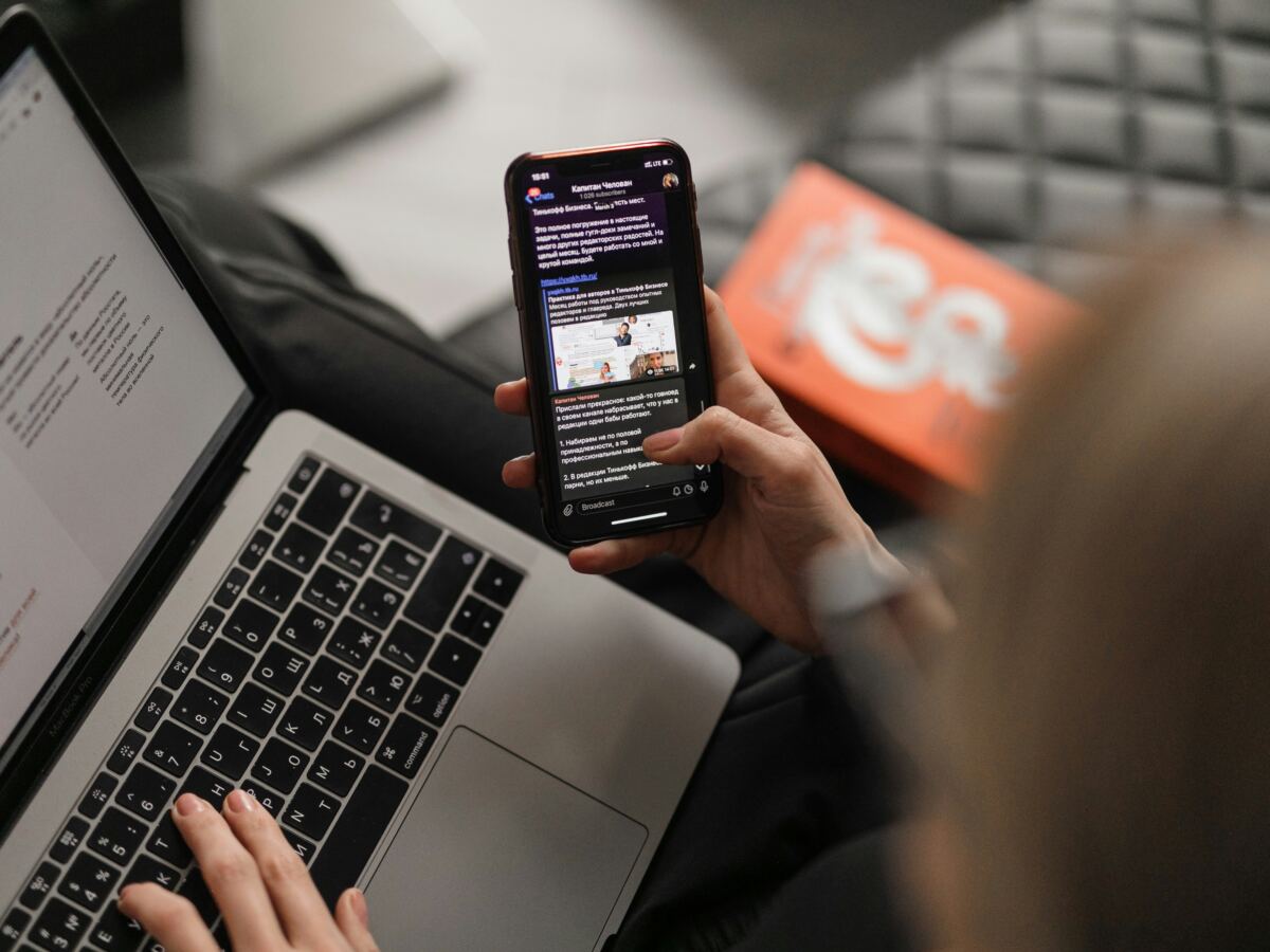 Person reading a news article on a phone beside a laptop