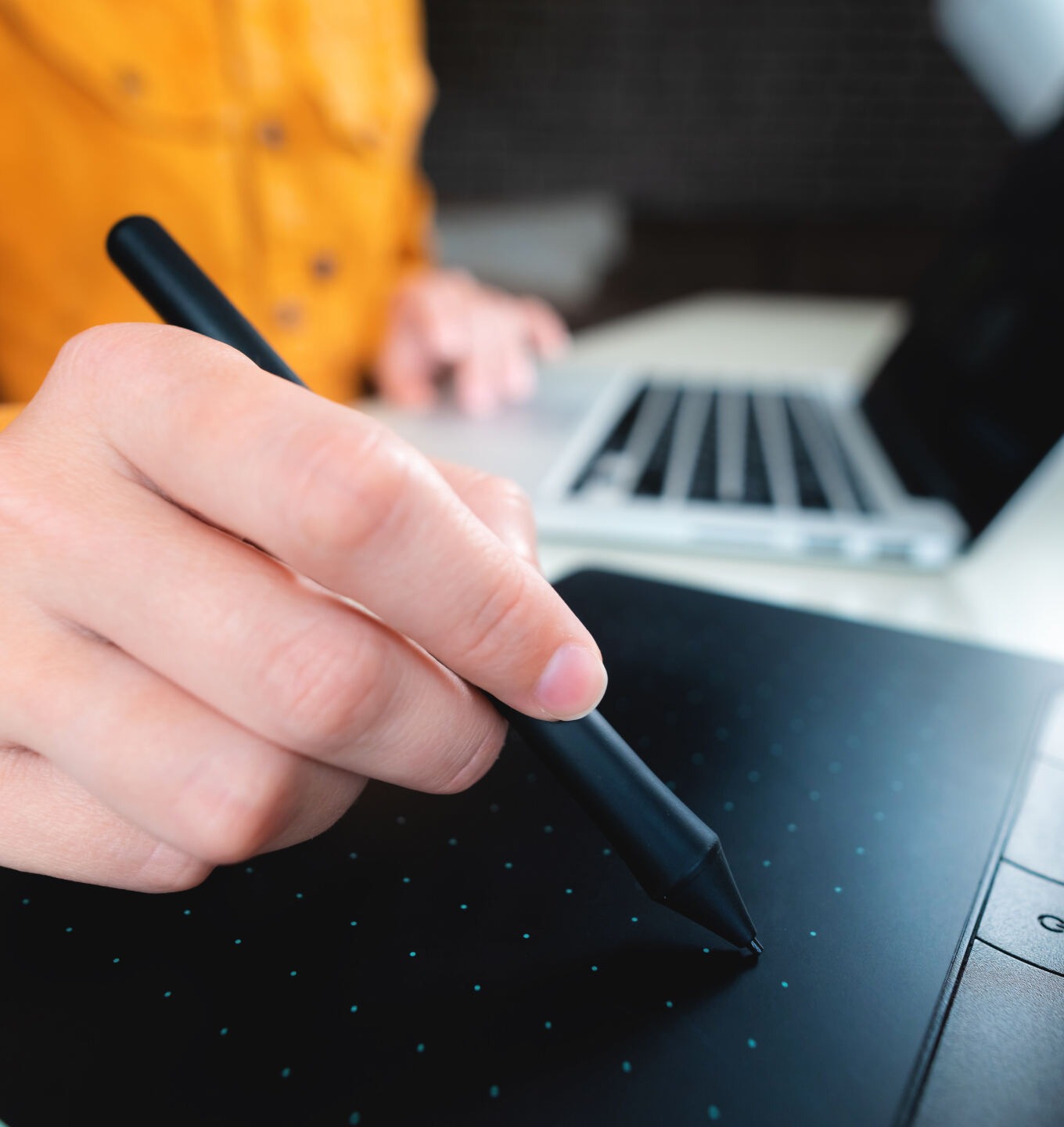 Web designer sketching on a graphics tablet with a stylus beside a laptop