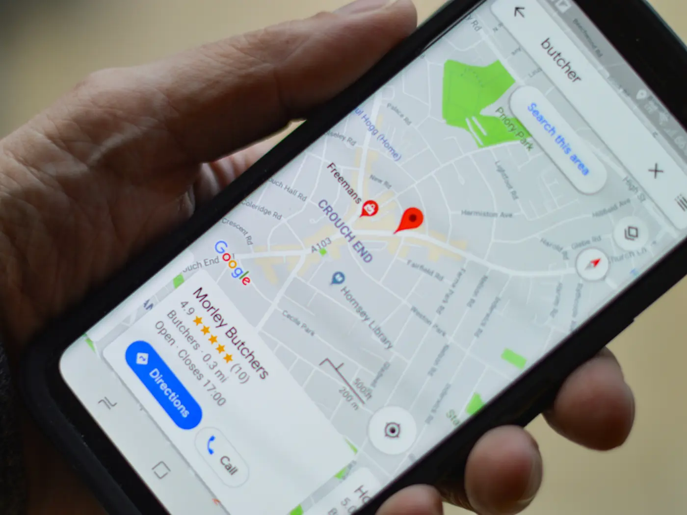 Hand holding a phone showing a local butcher on Google Maps with star rating, directions and call buttons