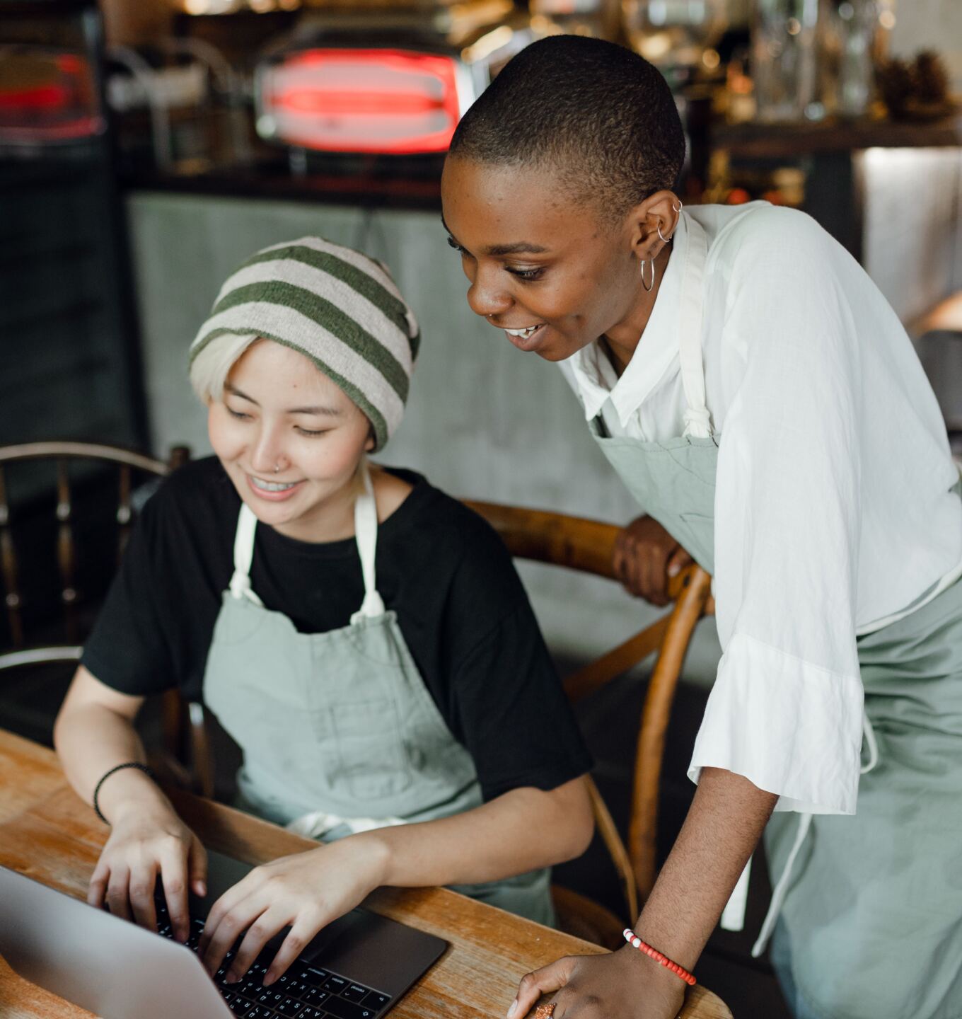 Two cafe owners in aprons smiling while working on a laptop together