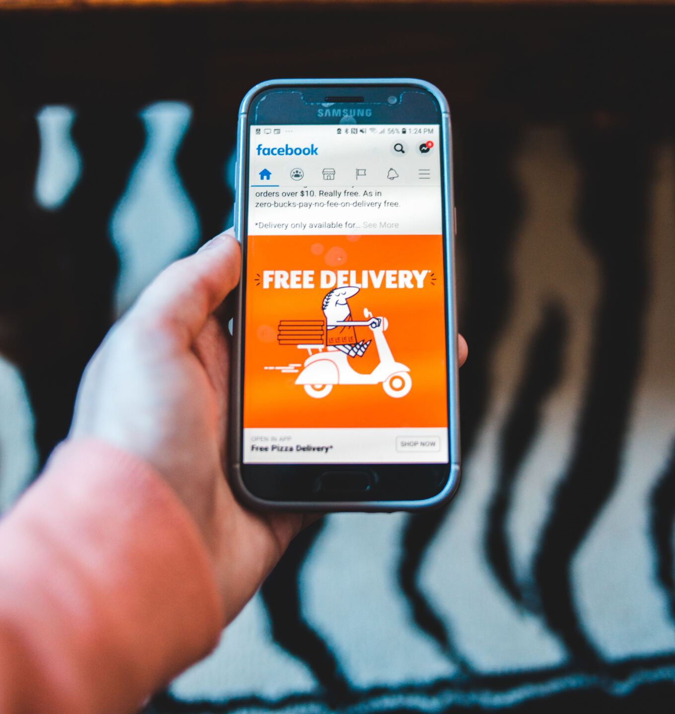 Hand holding a phone showing a free delivery ad in a social media feed