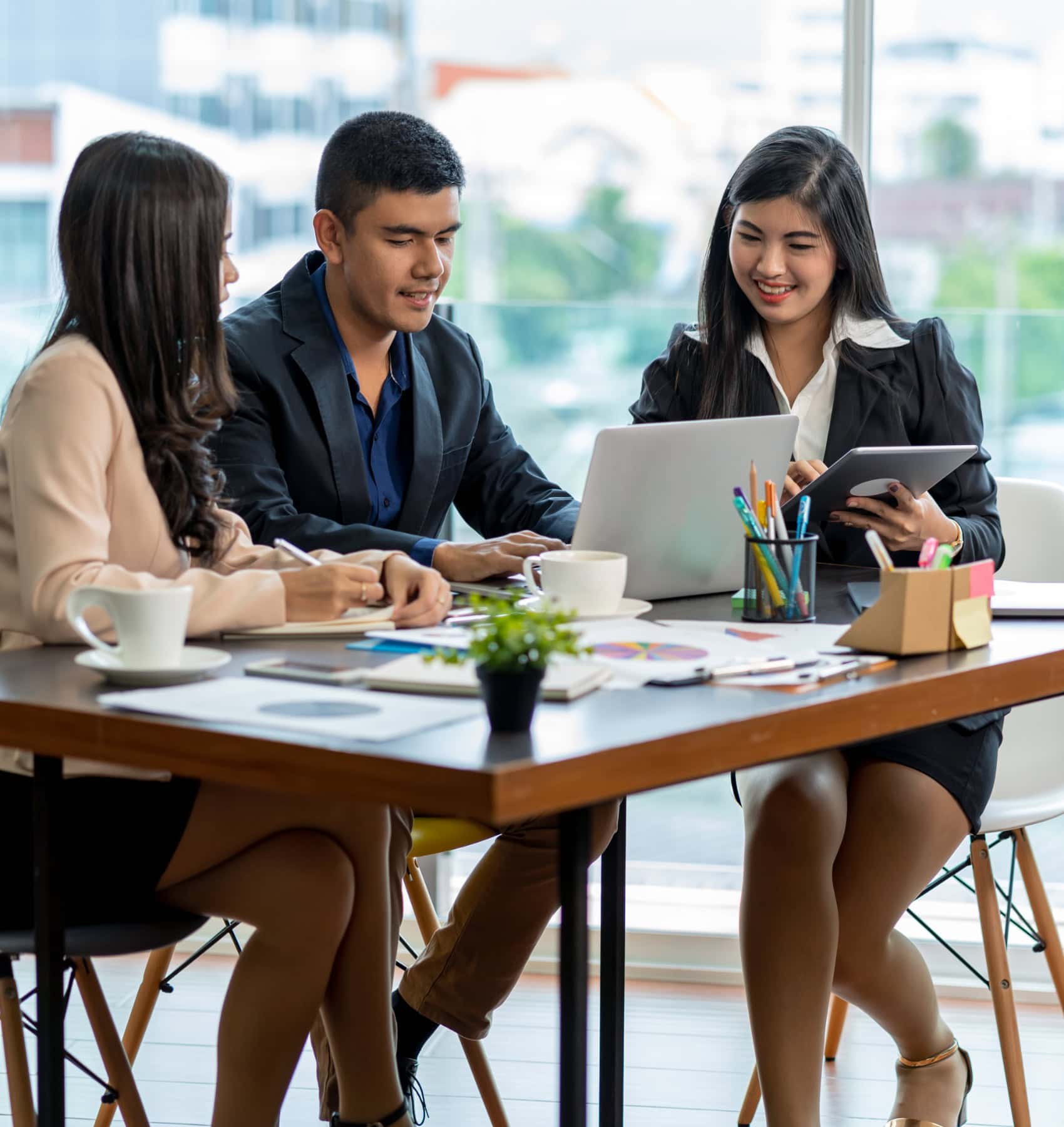 Team of three working together at a table with laptops and a tablet