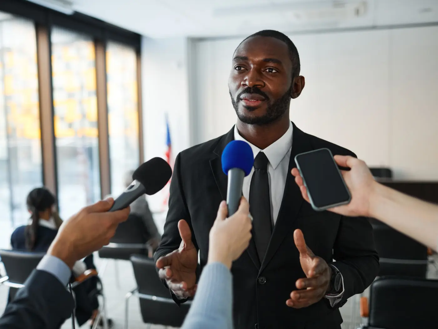 Business leader answering questions from journalists holding out microphones and phones