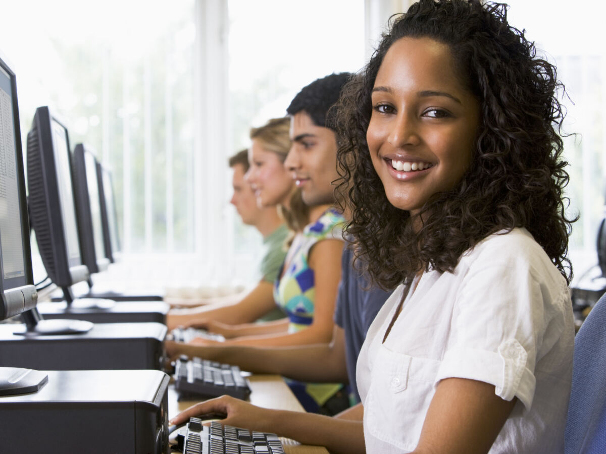Smiling woman at a computer terminal with colleagues working behind her