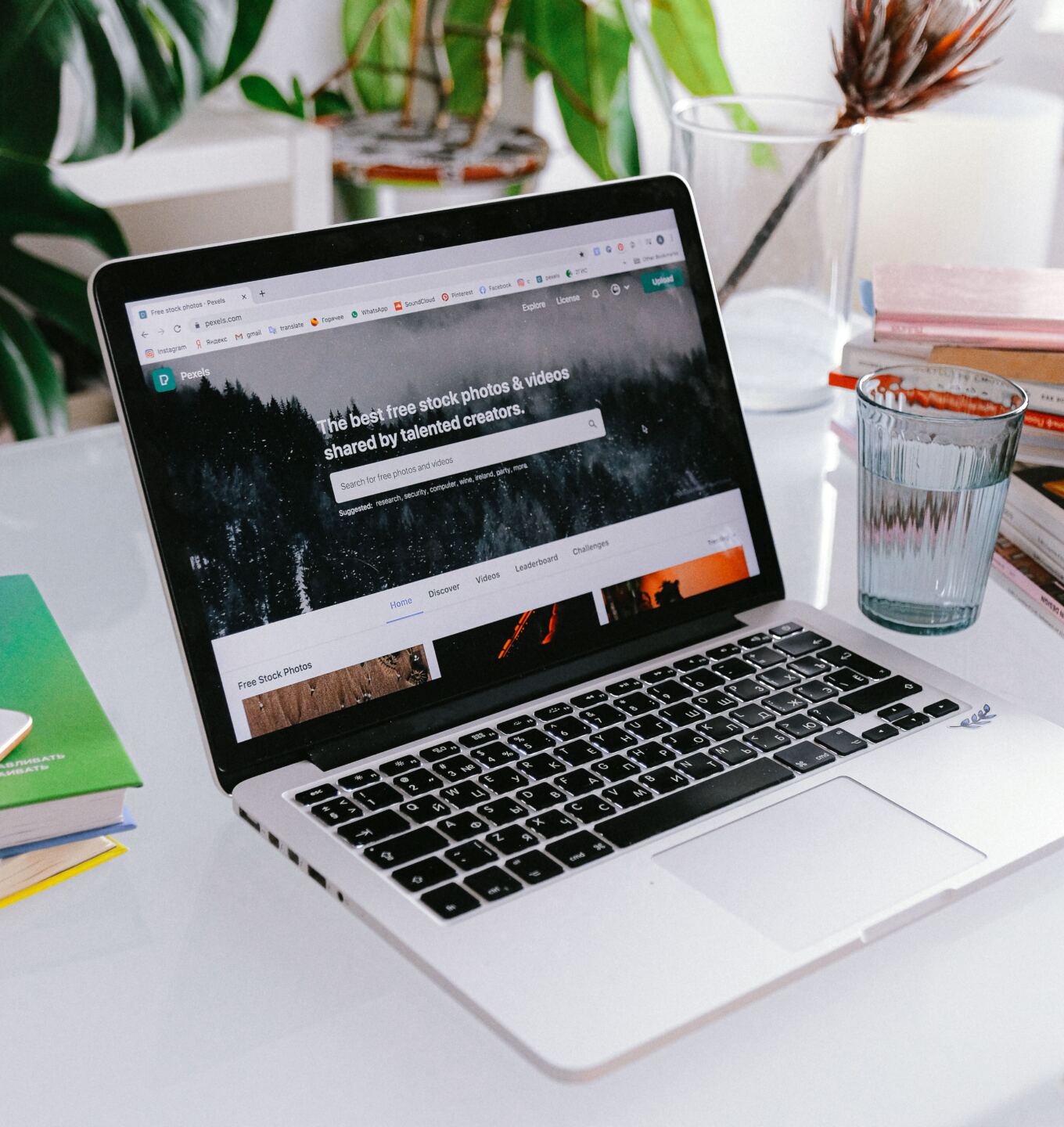 Laptop open on a white desk with plants and notebooks