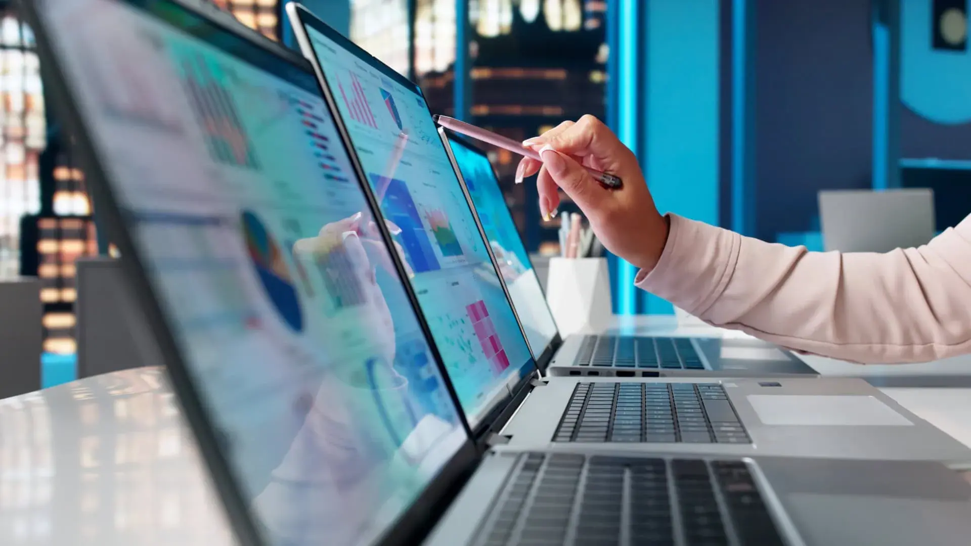 Hand pointing a pen at charts on a laptop screen