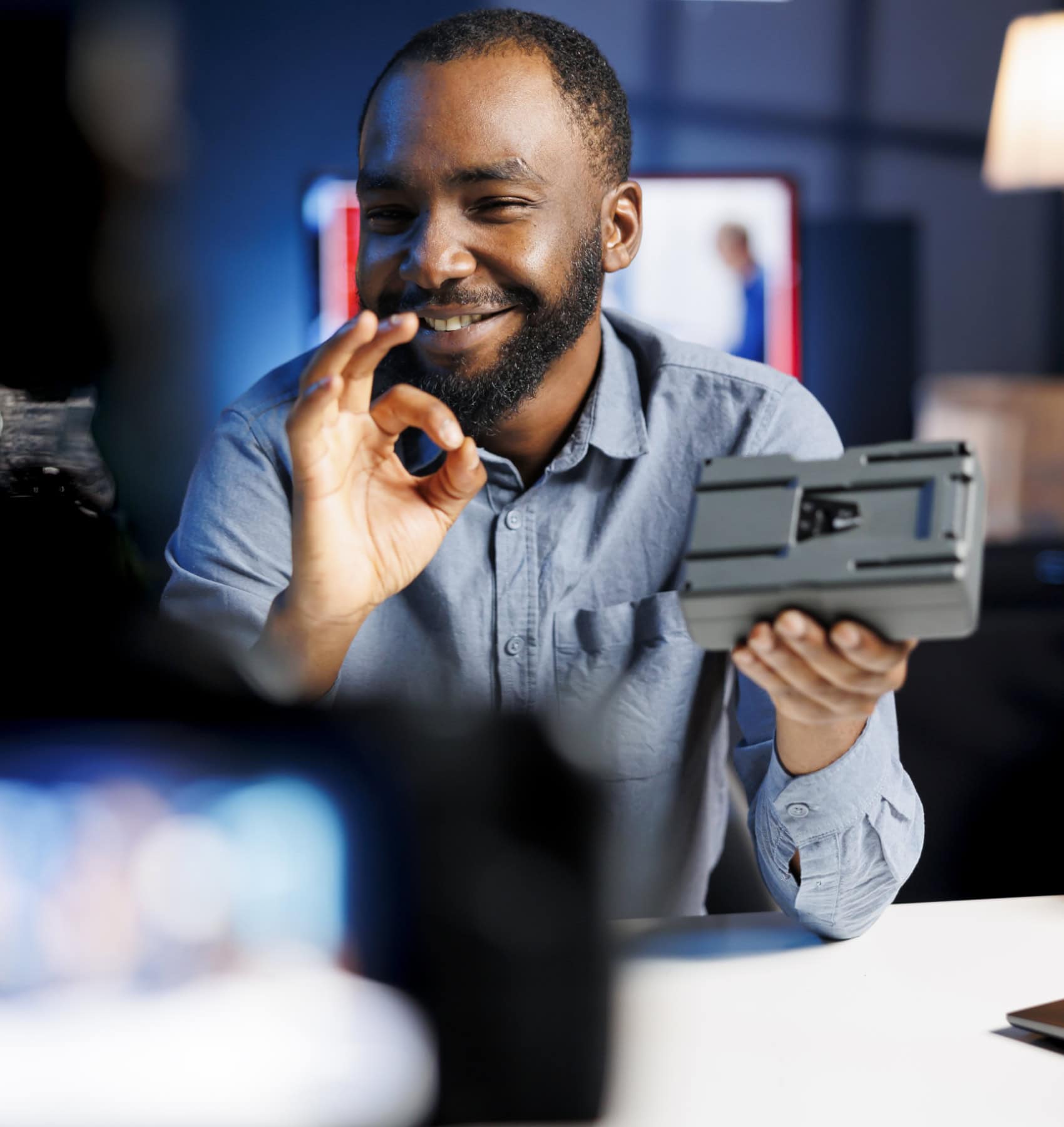Smiling videographer holding up camera gear and giving an OK sign in a studio