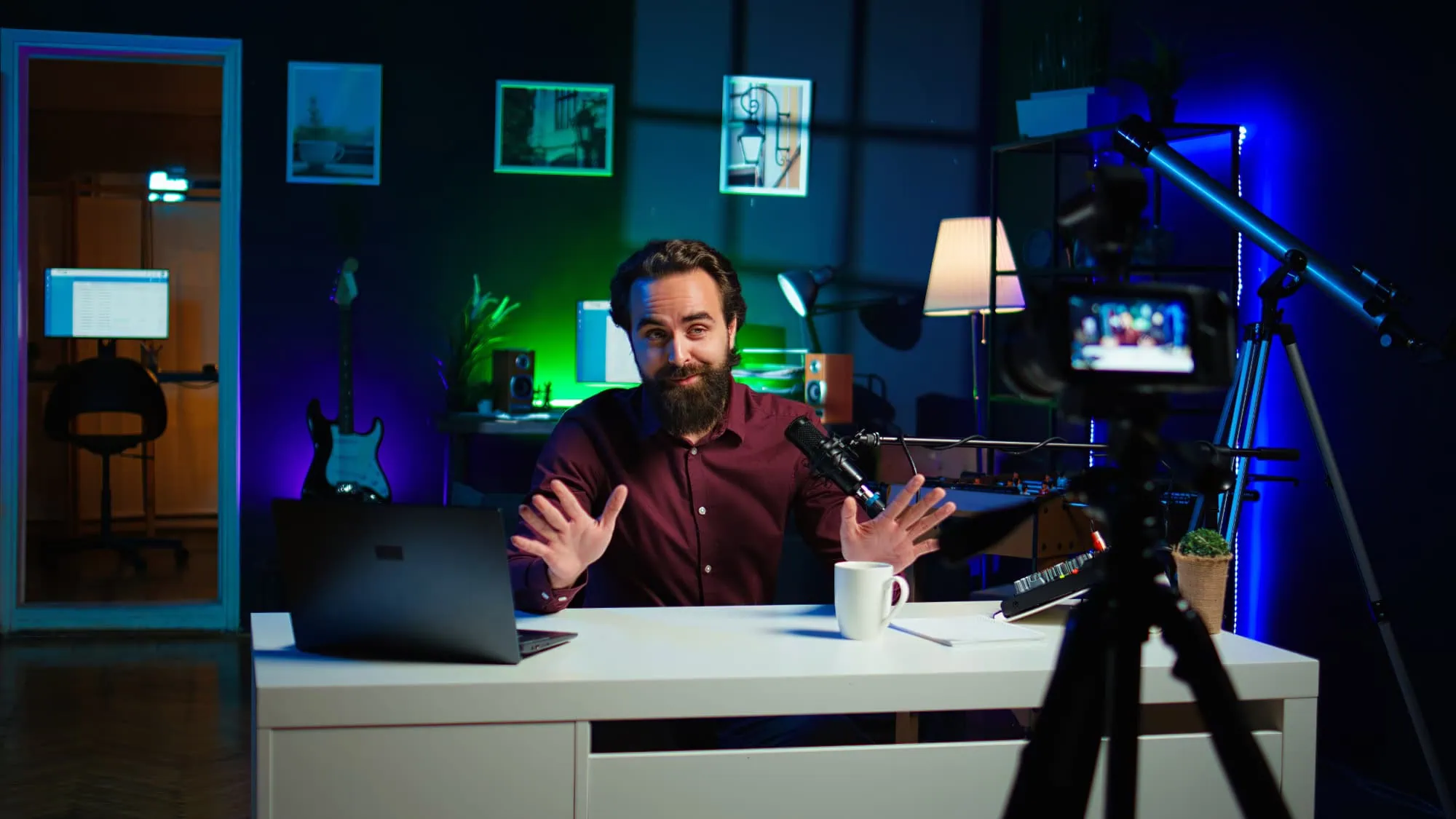 Presenter recording a video at a desk in a studio with a camera, microphone and coloured lighting