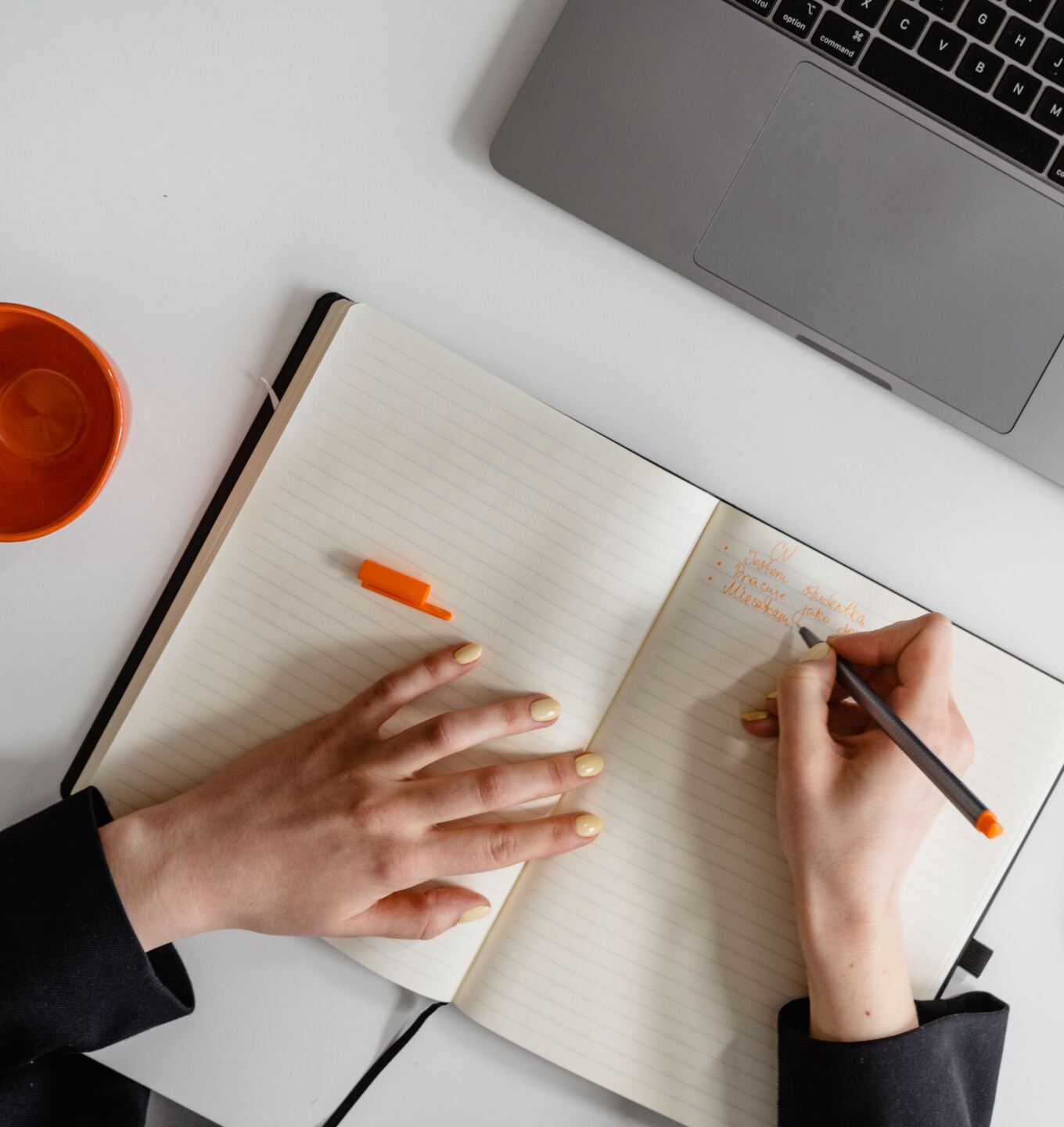 Person writing in a notebook beside an open laptop