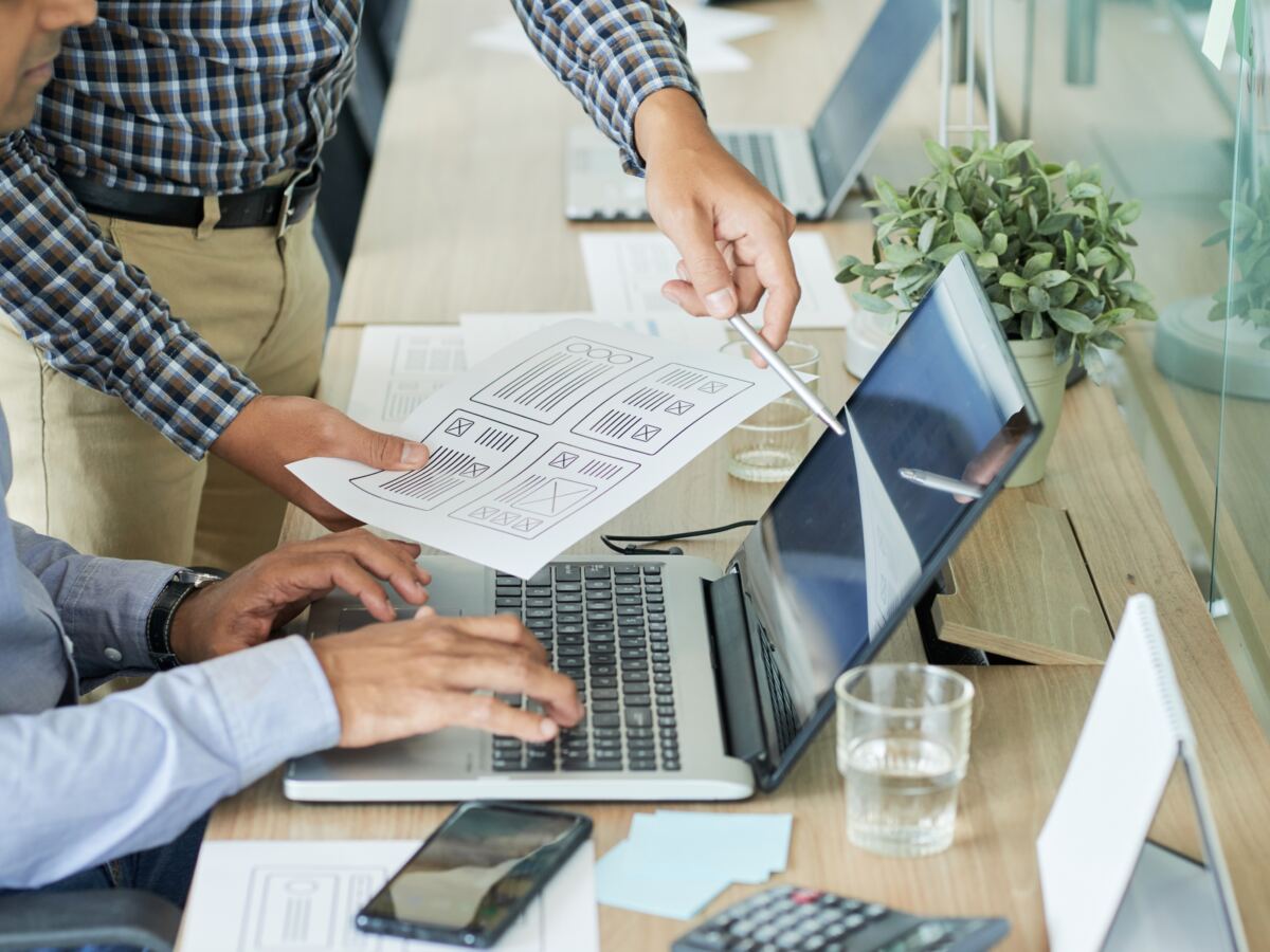 Designers reviewing printed page layouts beside a laptop